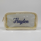 A clear pvc plastic cosmetic pouch with a cream-colored nylon border and a navy blue script name 'Hayden' printed on the front in permanent vinyl. zippered is gold 