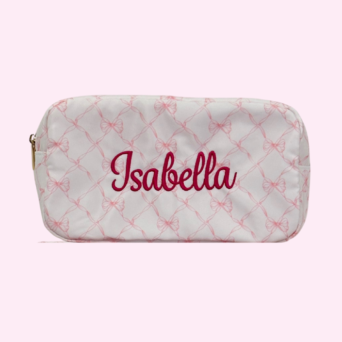 A personalized cosmetic pouch with the name 'Isabella' embroidered in pink on a white nylon bag with pink bows. zippered top pouch is a practical way to keep everything organized for travel or school. Matching backpack and large bag available. 